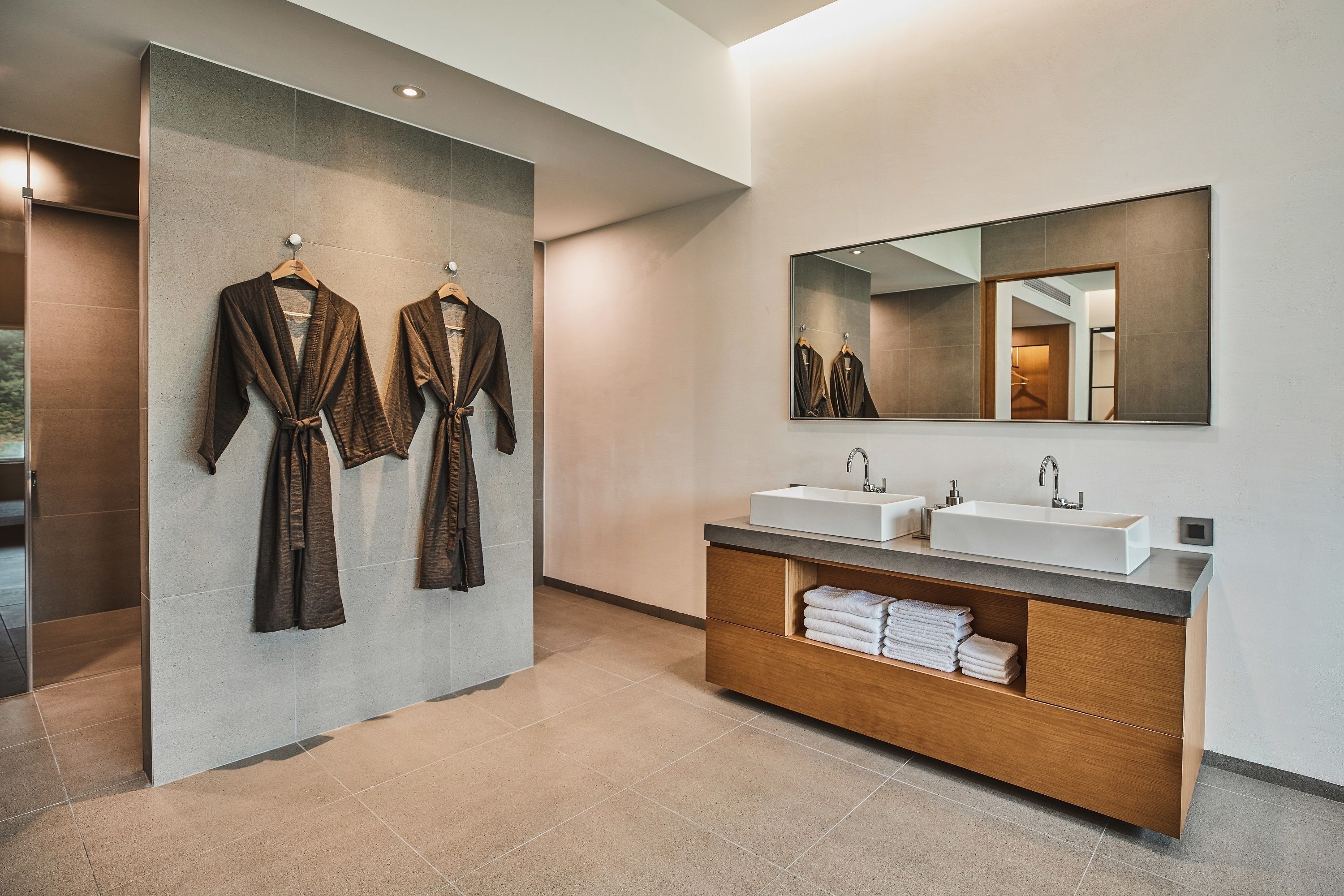 Un baño moderno con dos lavamanos, un espejo grande y albornoces colgados en la pared.