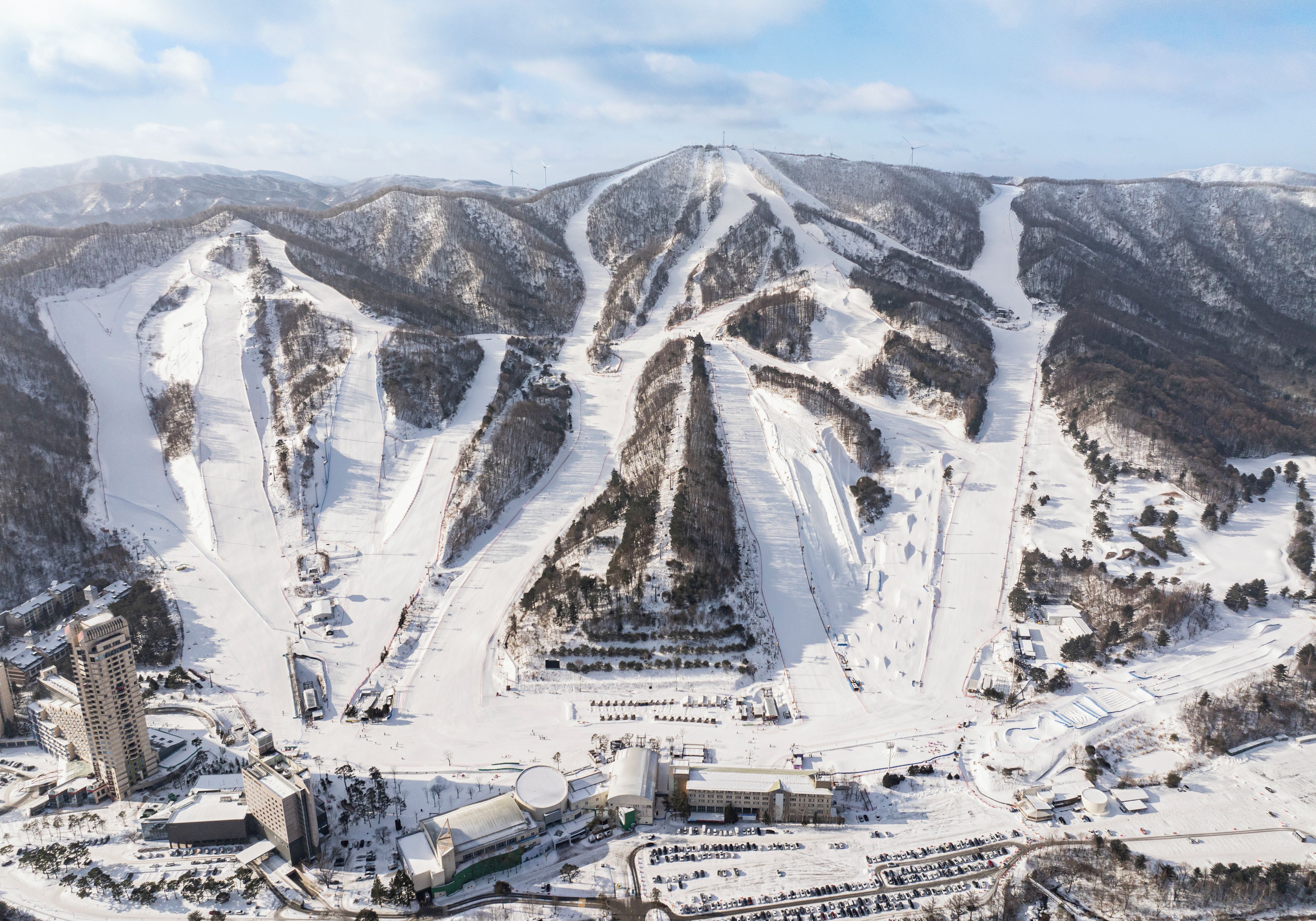 A snow-covered ski resort with multiple ski runs, buildings, and a parking area.