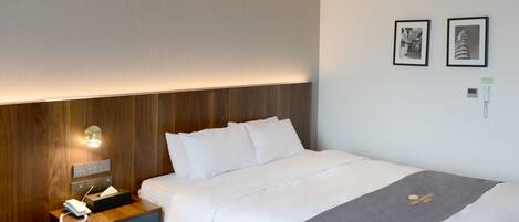 Una habitación de hotel con una cama bien hecha, una mesita de noche con lámpara y dos cuadros en la pared.