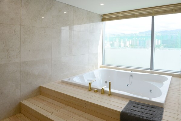 A modern bathroom with a large bathtub, wooden steps, and a view of a bridge and buildings. - Hotel Inter Burgo Wonju (Wonju)