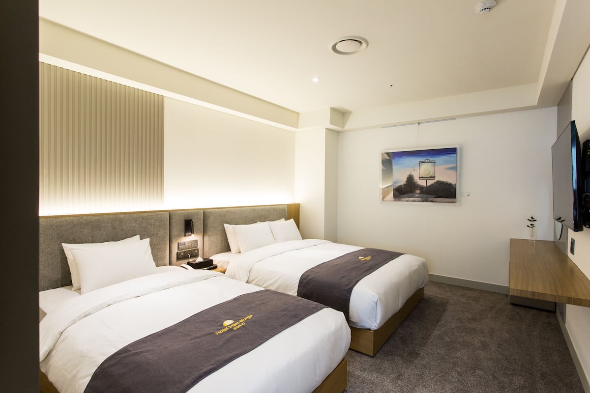 A hotel room with two beds, a nightstand, a flat-screen TV, and a painting on the wall.