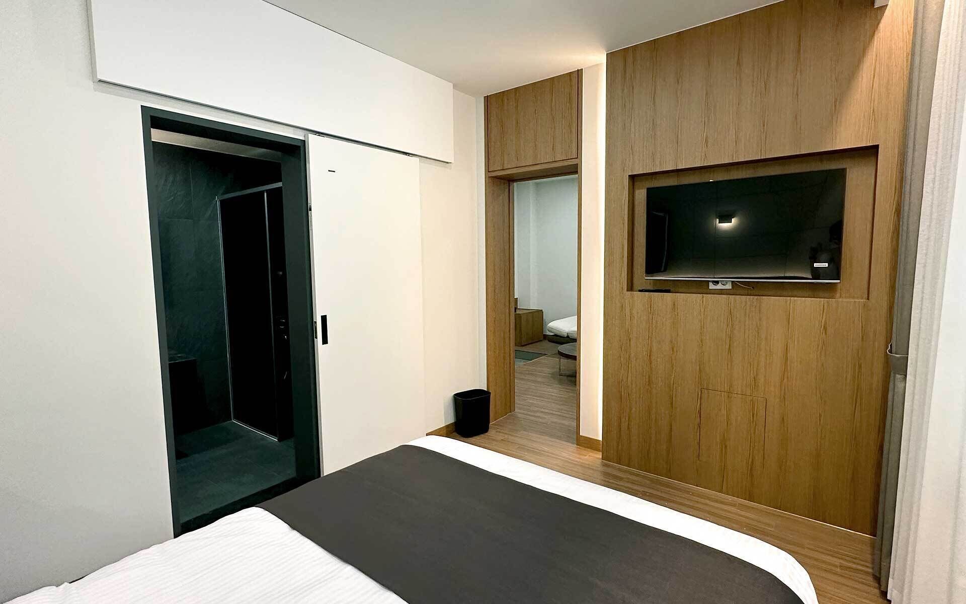 A modern hotel room with a bed, a TV mounted on the wall, and a wooden wardrobe.