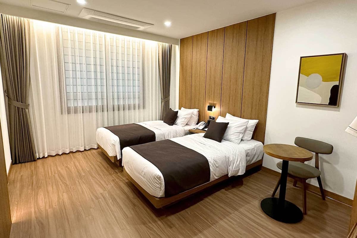 A hotel room with two beds, a small table, and a chair.