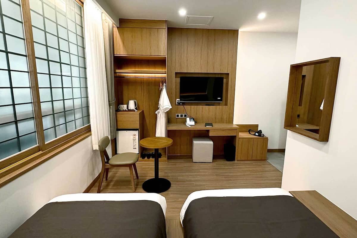 A compact hotel room with two single beds, a small desk with a chair, a television, and a mirror.
