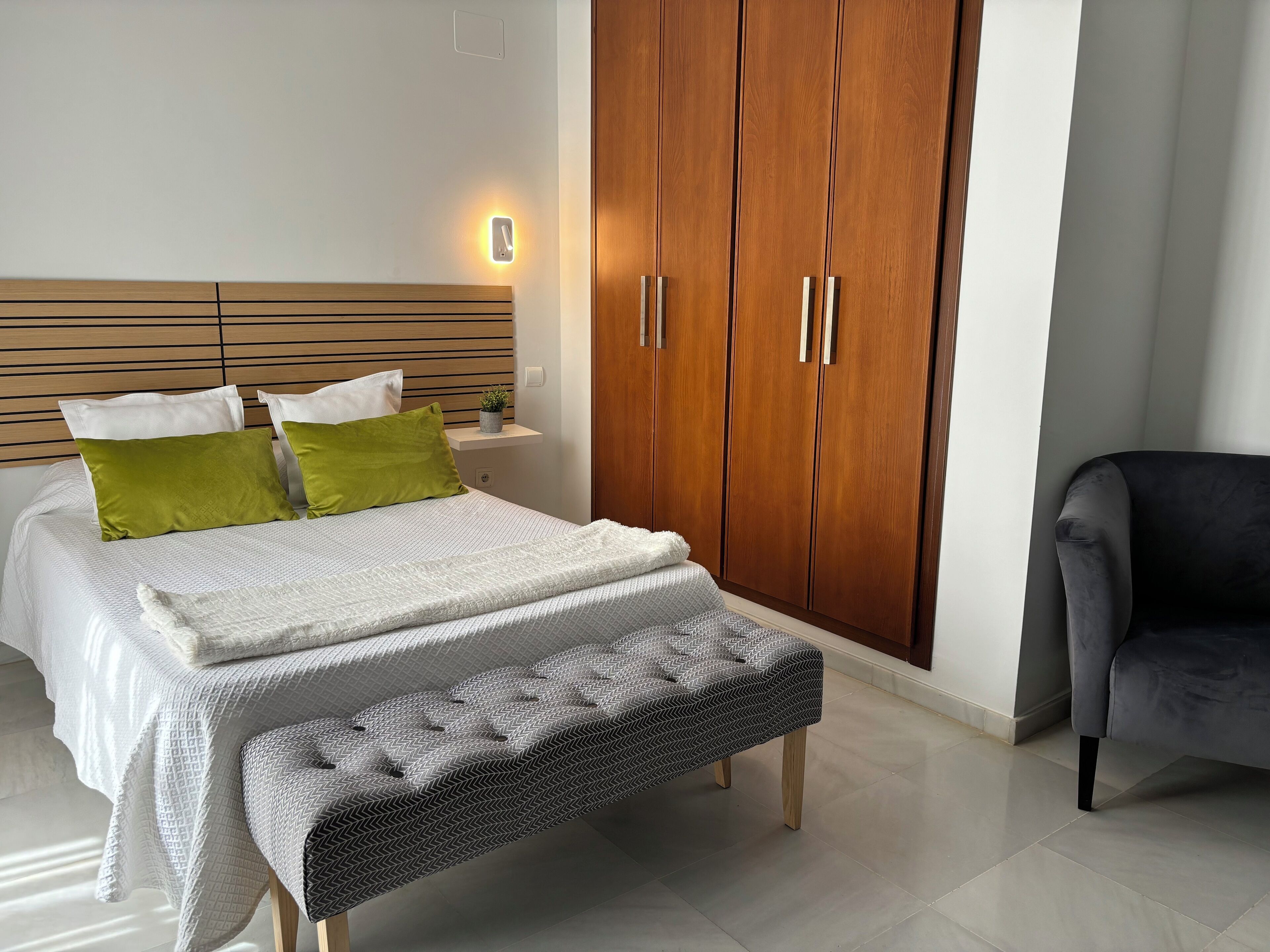 Un dormitorio con cama, banco, armario y silla.