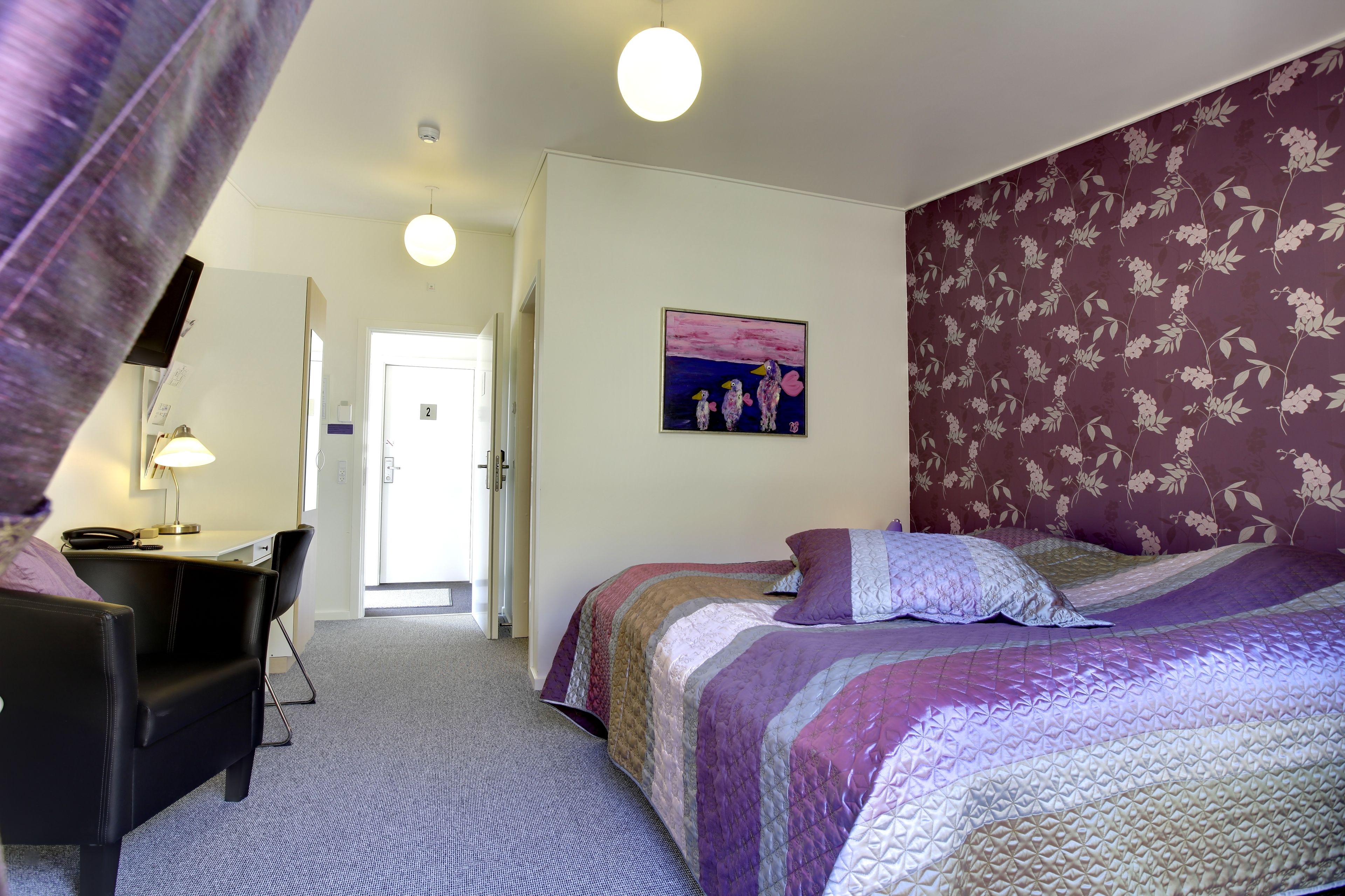 A bedroom with a bed, a desk, and a chair. There is a door leading to another room.