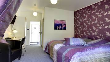 A bedroom with a bed, a desk, and a chair. There is a door leading to another room.