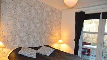 Un dormitorio con una pared estampada, una cama con dos almohadas, dos lámparas de noche y una ventana con cortinas.