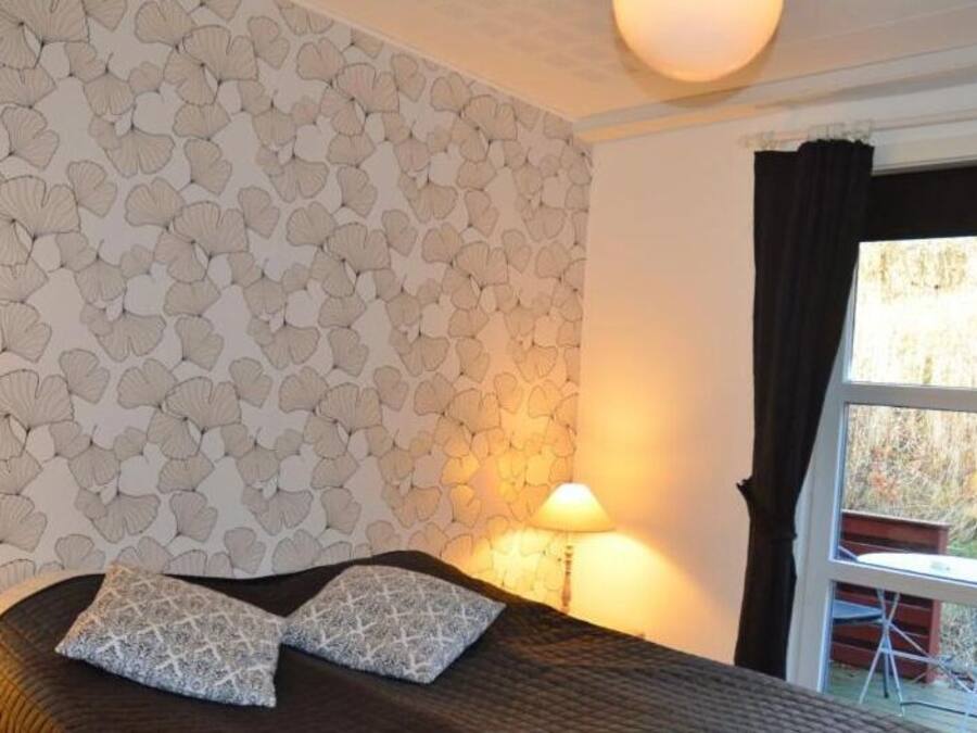 Un dormitorio con una pared estampada, una cama con dos almohadas, dos lámparas de noche y una ventana con cortinas.