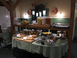 Una mesa con una variedad de alimentos y bebidas en estilo bufé, rodeada de sillas y una pared con diseño.
