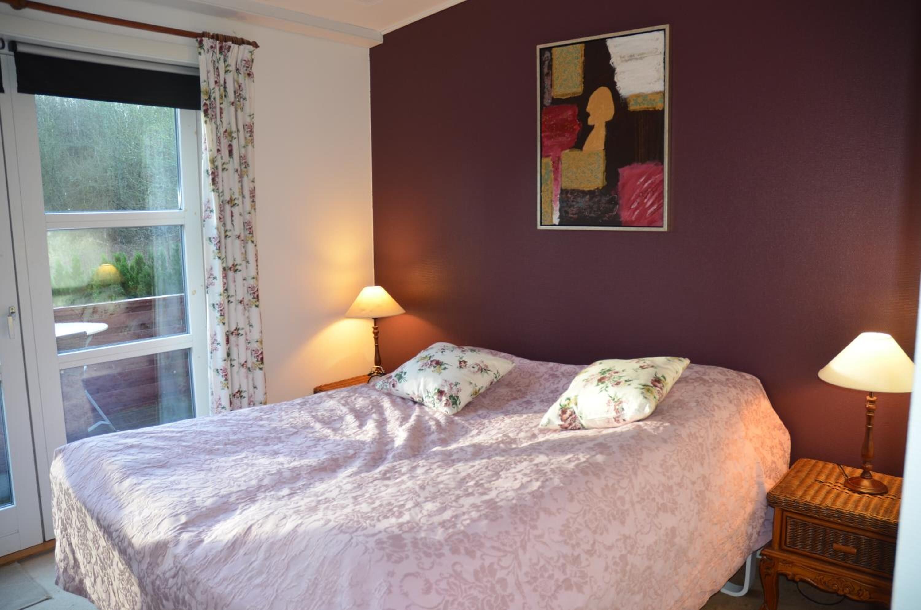 Une chambre à coucher avec un lit, deux lampes de chevet, une fenêtre avec des rideaux et un tableau au mur.