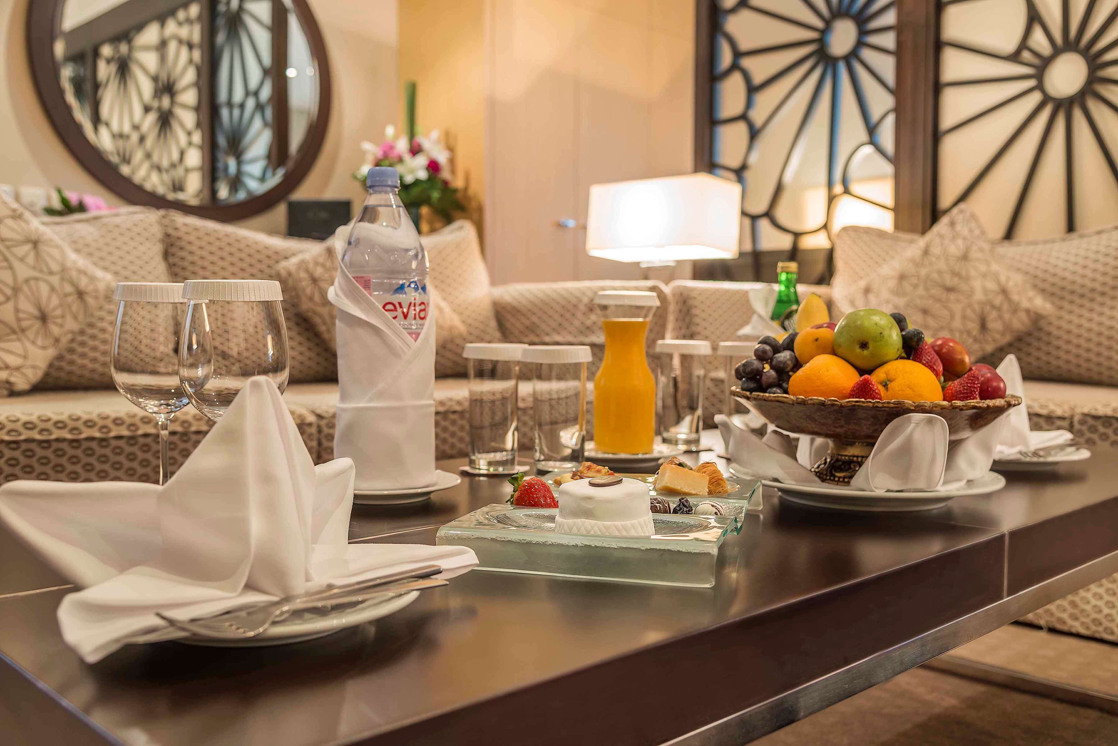 Une table mise pour le petit-déjeuner, avec un panier de fruits, du jus et un gâteau.