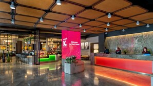 Zona de recepción de hotel con diseño moderno, que incluye una gran pantalla digital de bienvenida, un mostrador de recepción y un área de descanso con sillas y una pequeña mesa.