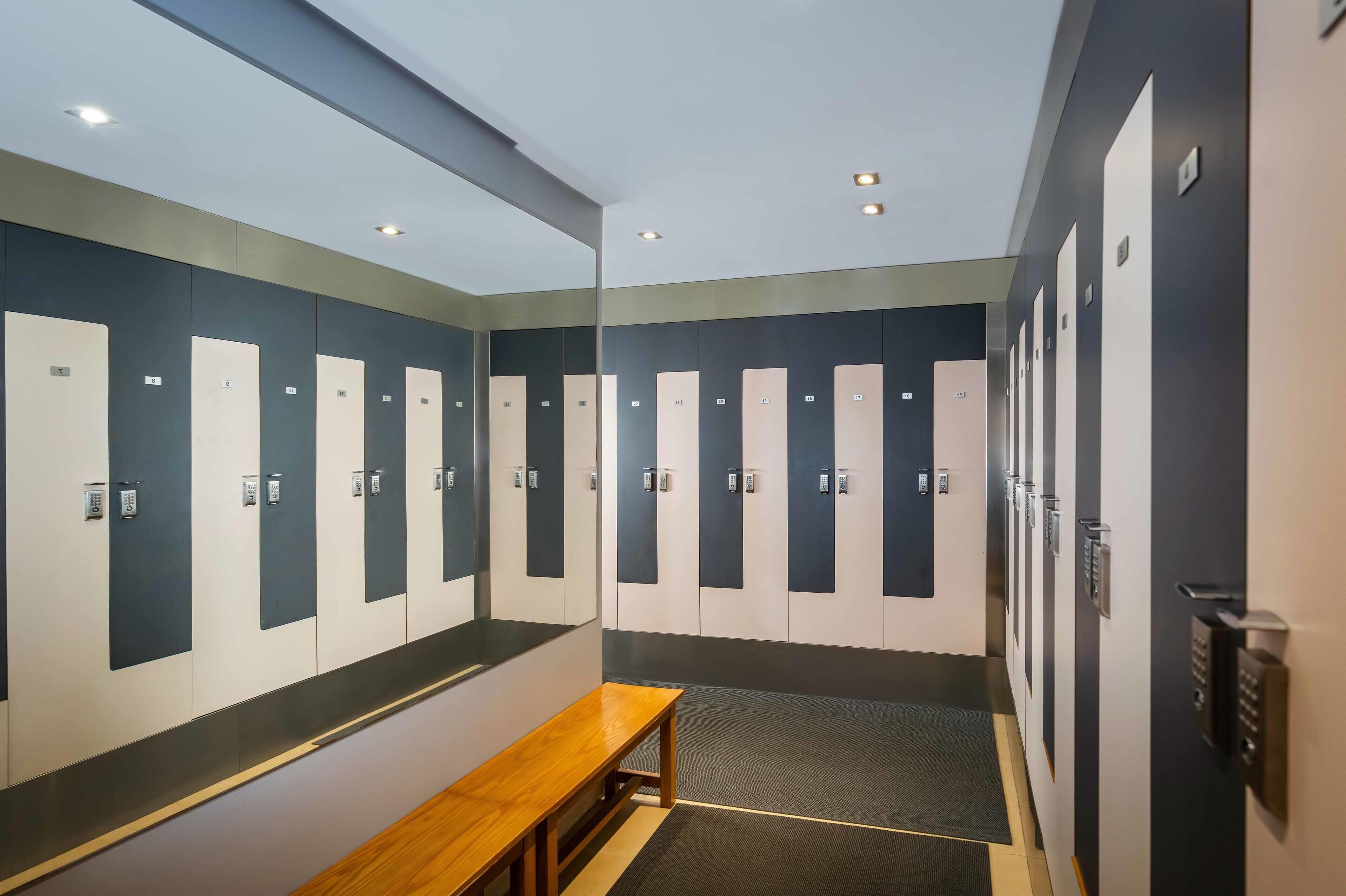 A modern locker room with multiple lockers, a bench, and a wall-mounted control panel.