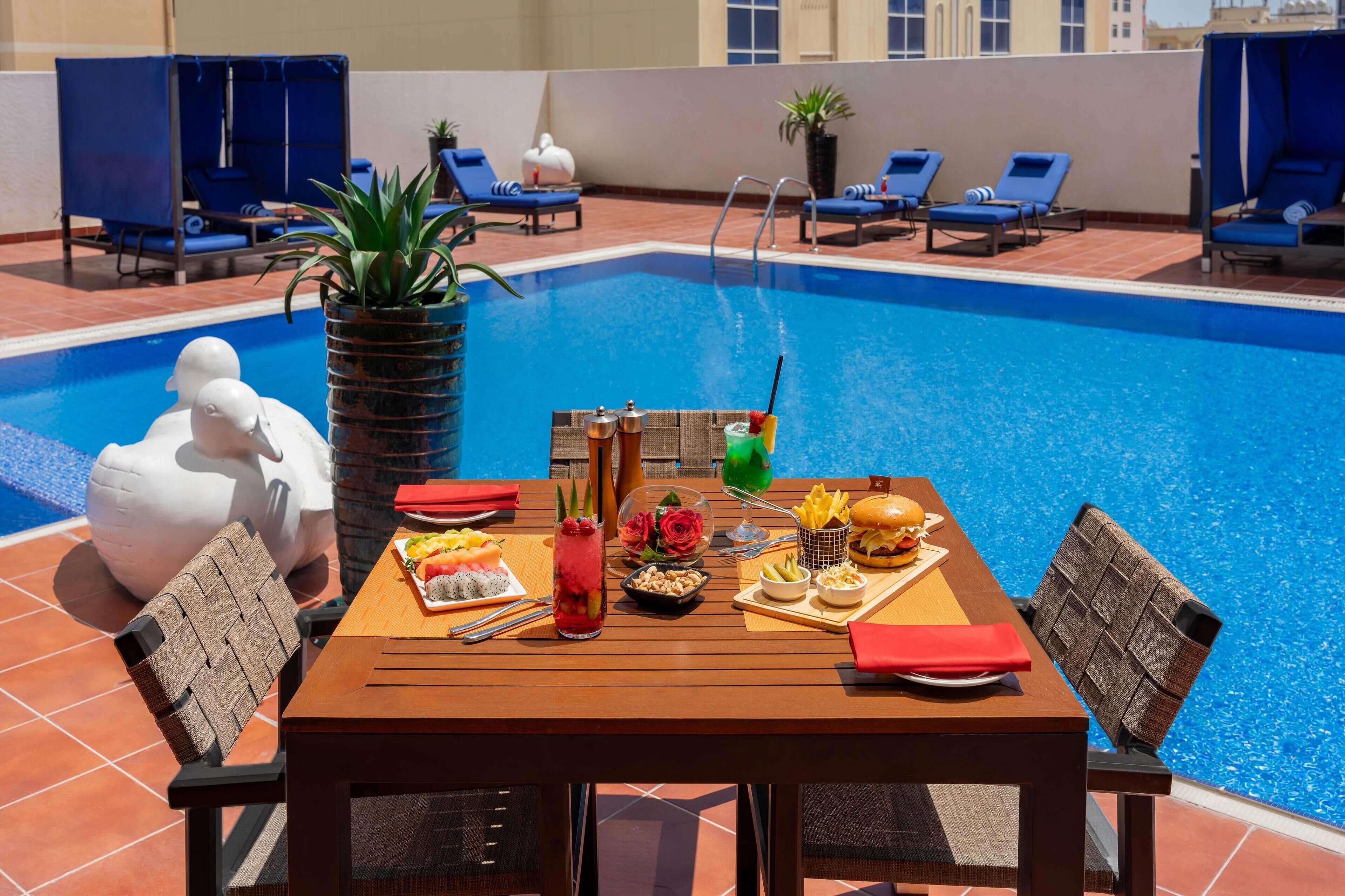 A poolside dining area with a table set for two, a pool, and lounge chairs.