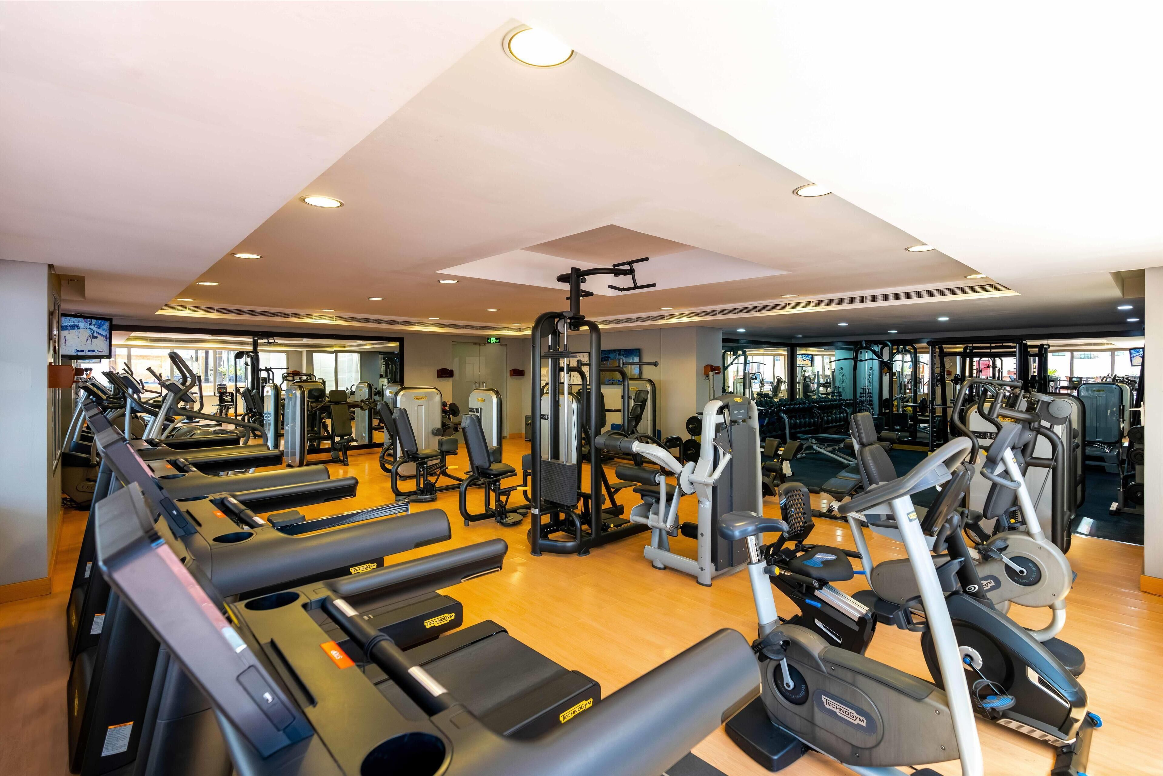 Une salle de sport équipée de plusieurs tapis de course, de plusieurs appareils de musculation elliptique et de matériel de musculation.