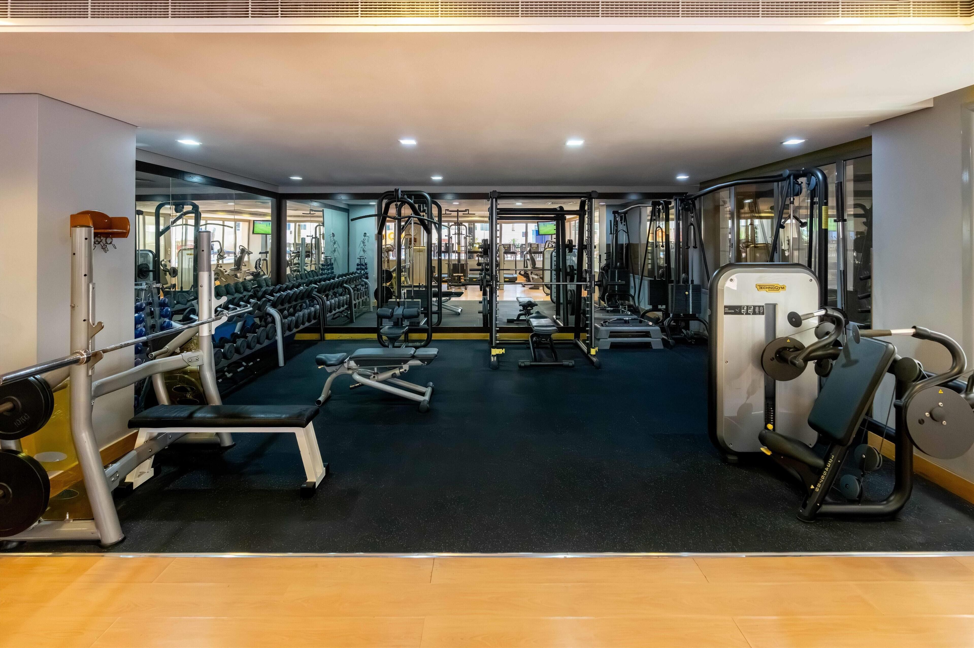 Un gimnasio con varios equipos de ejercicio, entre ellos máquinas de pesas, bancos y mancuernas.