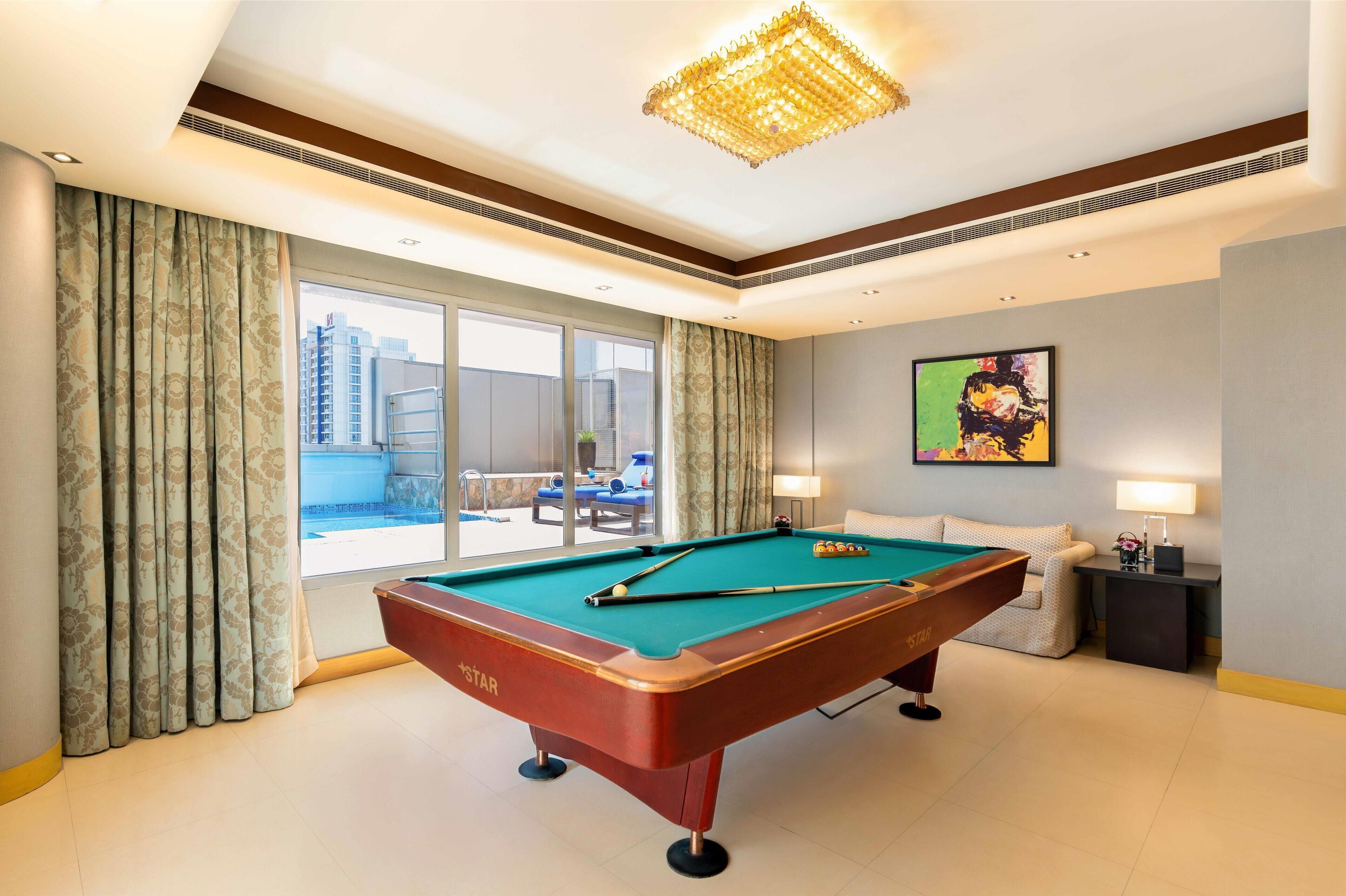 A hotel room with a pool table, a sofa, a chair, a lamp, and a painting on the wall.
