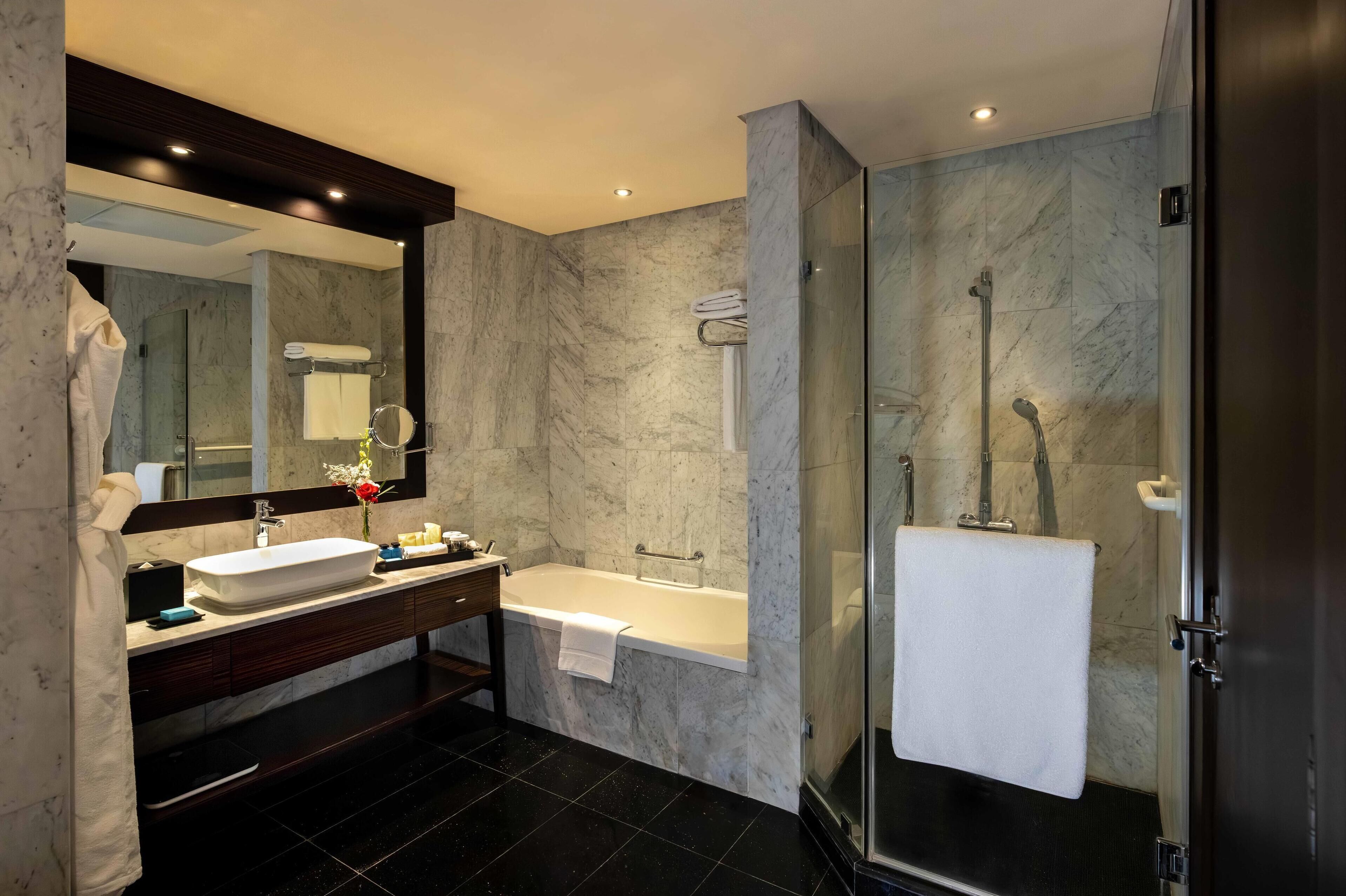 A modern bathroom with a large mirror, a sink, a bathtub, and a glass-enclosed shower.