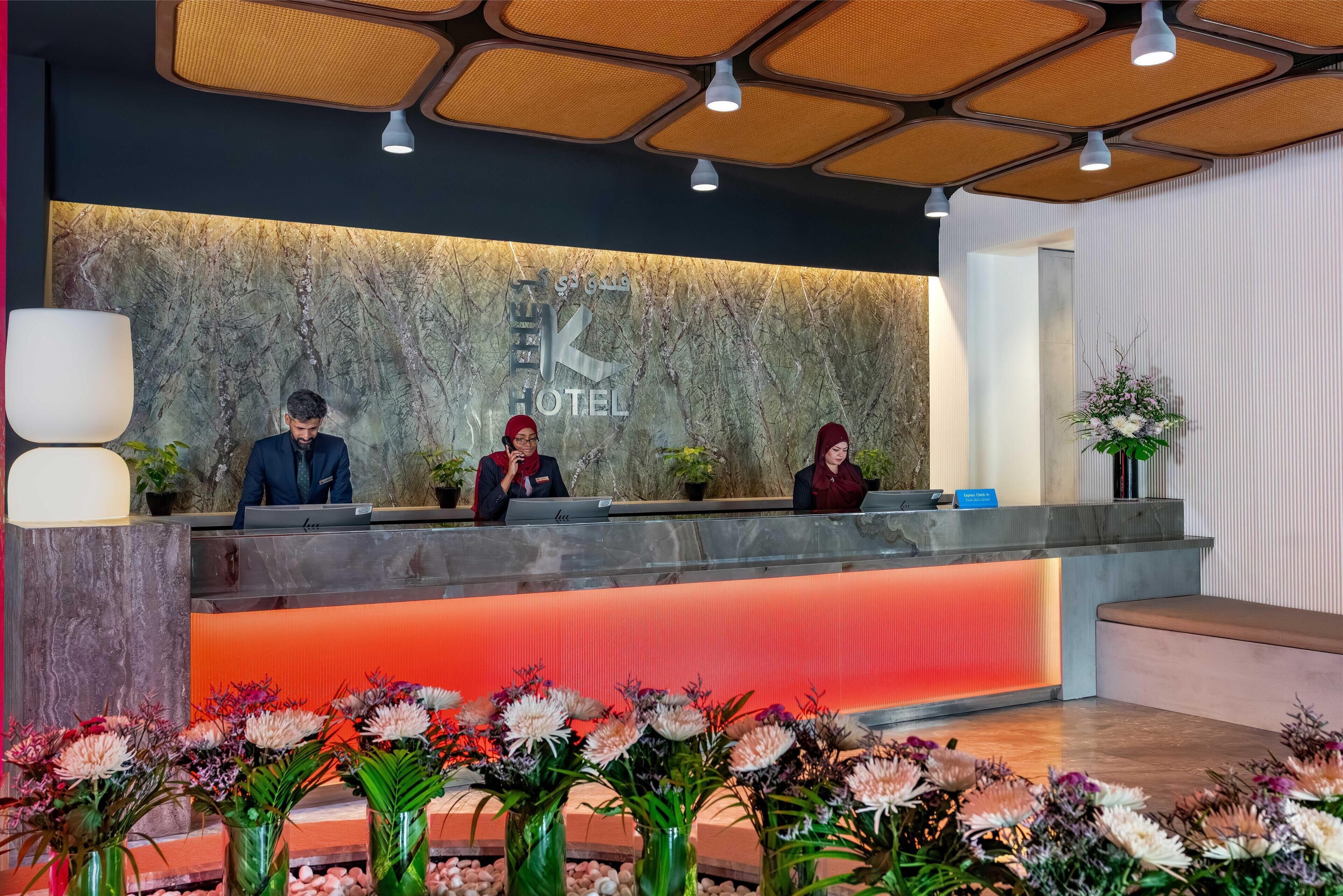 En hotelfri reception med tre medarbejdere, en marmorvæg med hotellets navn og en bordplade i rødt lys.