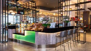 Una cafetería moderna con mostrador de mármol, taburetes de bar y una variedad de pasteles y flores.