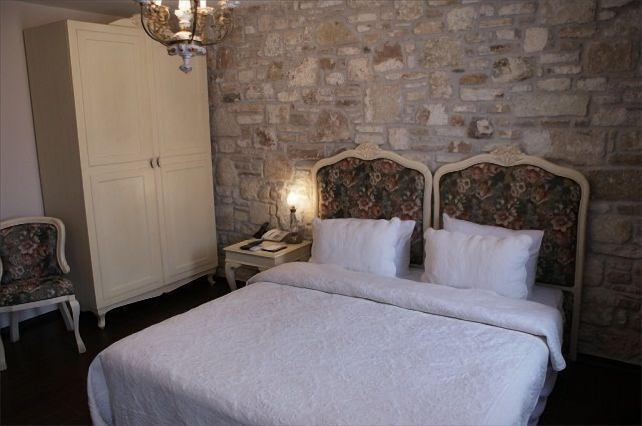 A bedroom with a large bed, a nightstand, a telephone, and a chair.