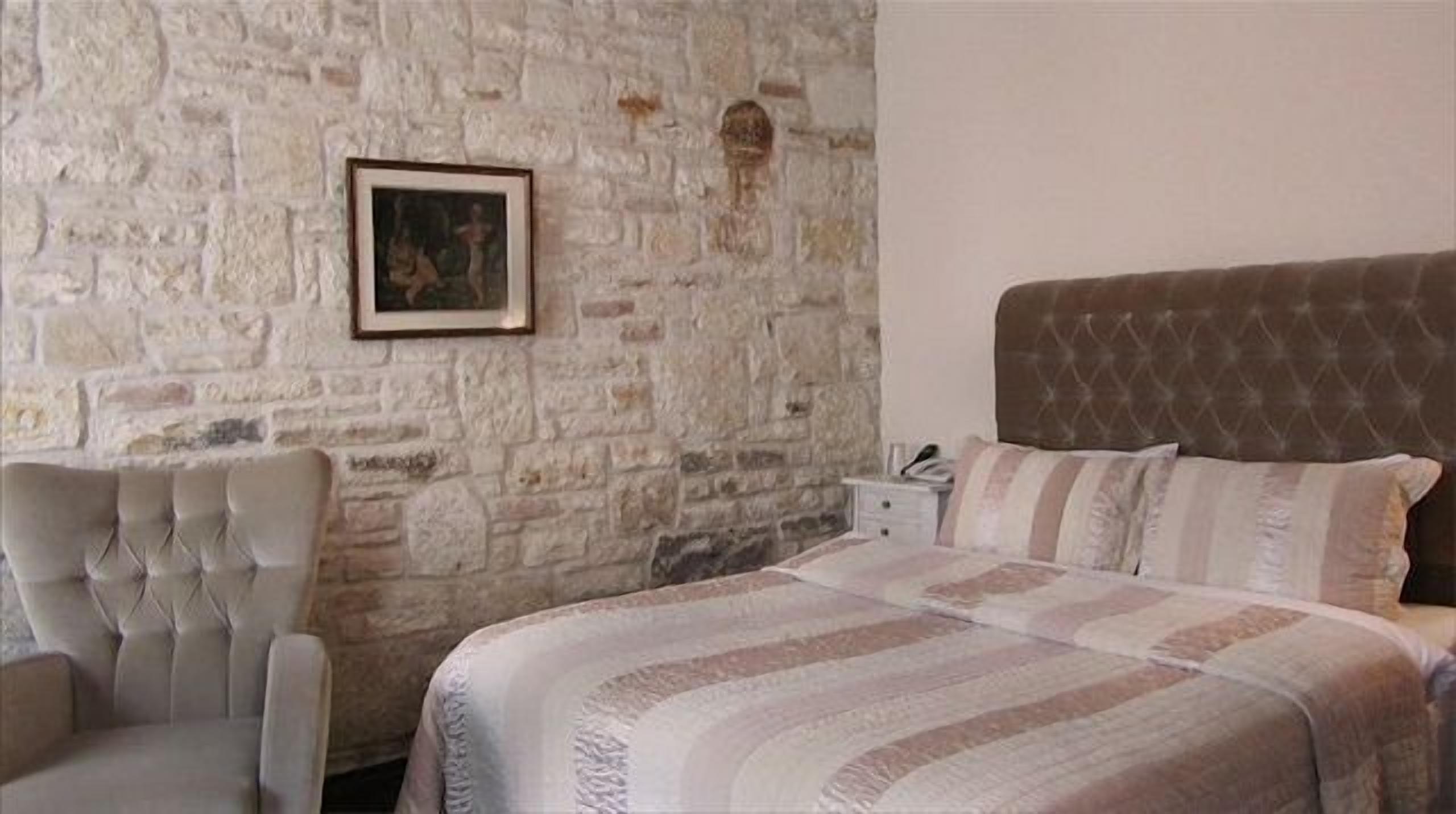 Un dormitorio con pared de piedra, cabecera capitonada, cama con ropa de cama a rayas y un cuadro enmarcado en la pared.