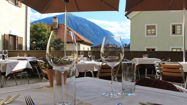 Ein Essbereich im Freien mit Tischen für zwei Personen, ausgestattet mit sauberem Glas und Besteck.