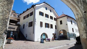 Ein historisches Gebäude mit weißer Fassade und roten Ziegeldach, das einen zentralen Innenhof mit Kopfsteinpflaster und einem Bogen zeigt.