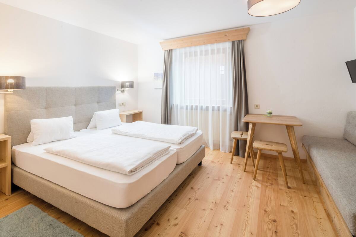 A hotel room with a large bed, bedside tables, a desk, and a sofa.