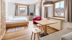 Ein modernes Zimmer mit Bett, einem roten Sessel, einem Tisch und Blick auf einen Berg.