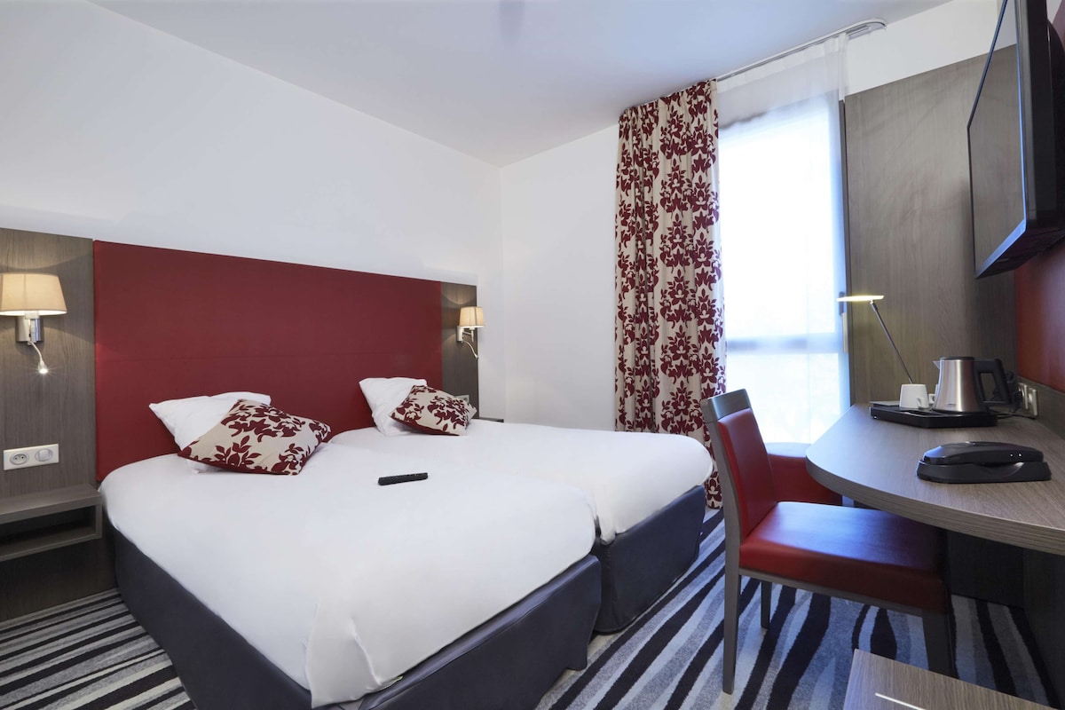 Habitación de hotel con una cama doble, un escritorio con silla, televisión y ventana con cortinas.