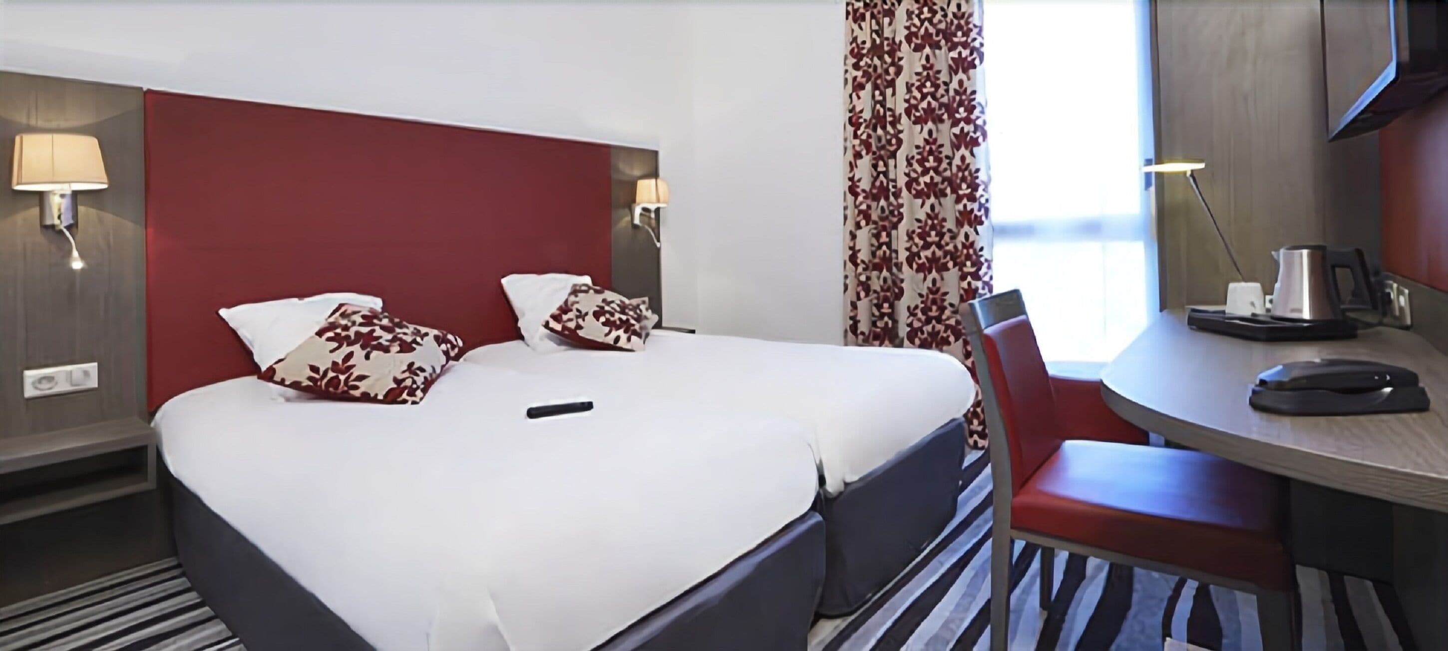 Une chambre d’hôtel avec un lit, un bureau et une chaise. Il y a deux tables de chevet avec des lampes.