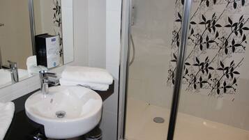 Een badkamer met een witte wastafel, een spiegel en een douche met glazen wanden.