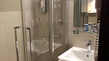 Een moderne badkamer met een douchecabine van glas, een witte wastafel en een spiegel erboven.