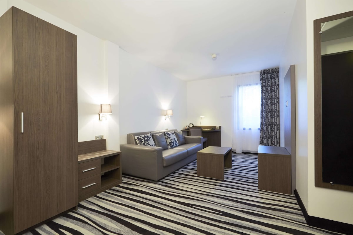 Habitación de hotel con sofá, mesa de centro, televisor, armario y alfombra a rayas.