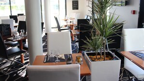 A restaurant with tables set for dining, chairs, and a potted plant. - Hôtel Kyriad Saint Quentin en Yvelines - Montigny (Montigny-le-Bretonneux)
