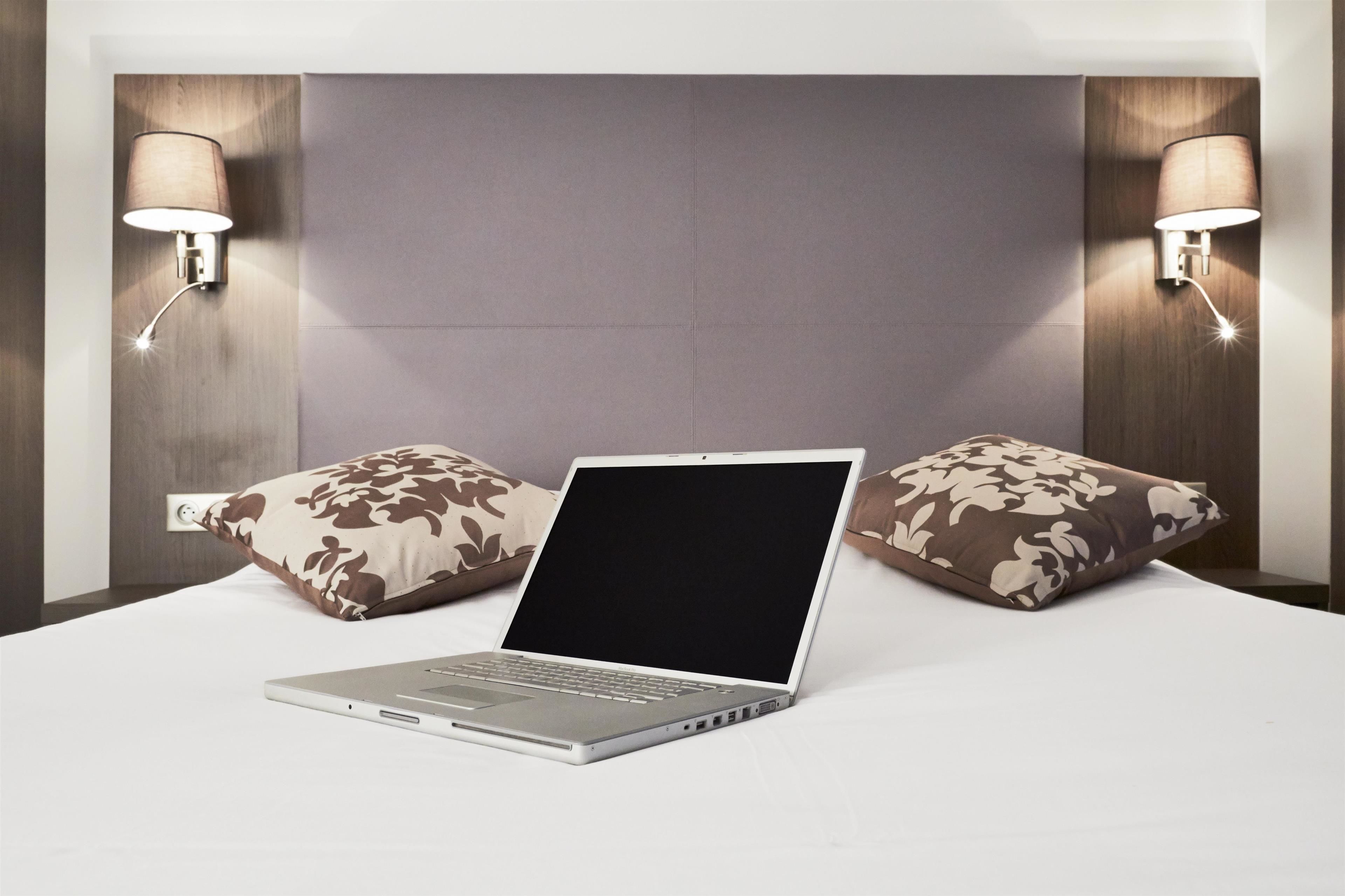 Een laptop op een bed met twee gestreepte kussens en twee wandlampen.