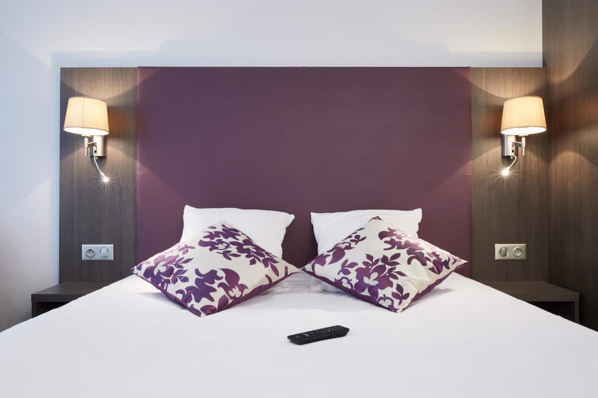 Ein Hotelzimmer mit einem Bett, zwei Nachttischen, einer Fernbedienung und Wandleuchten.