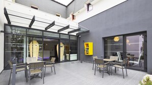 An outdoor seating area with modern furniture and a glass enclosure. - Hôtel Kyriad Saint Quentin en Yvelines - Montigny (Montigny-le-Bretonneux)