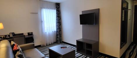 A hotel room with a sofa, a coffee table, a TV, and a striped carpet.