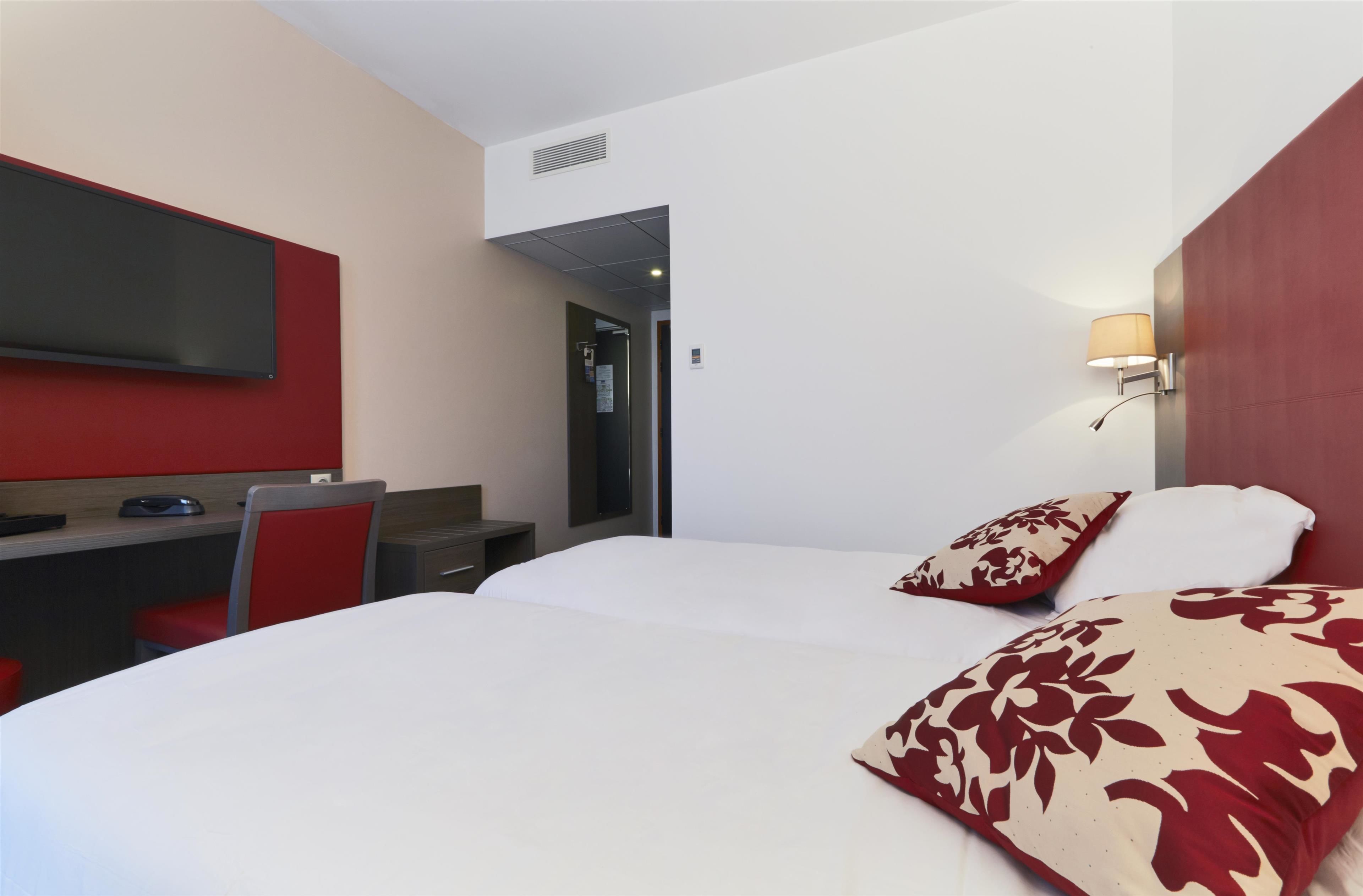 Ein Hotelzimmer mit Bett, Schreibtisch, Stuhl, Wandfernseher und Lampe.