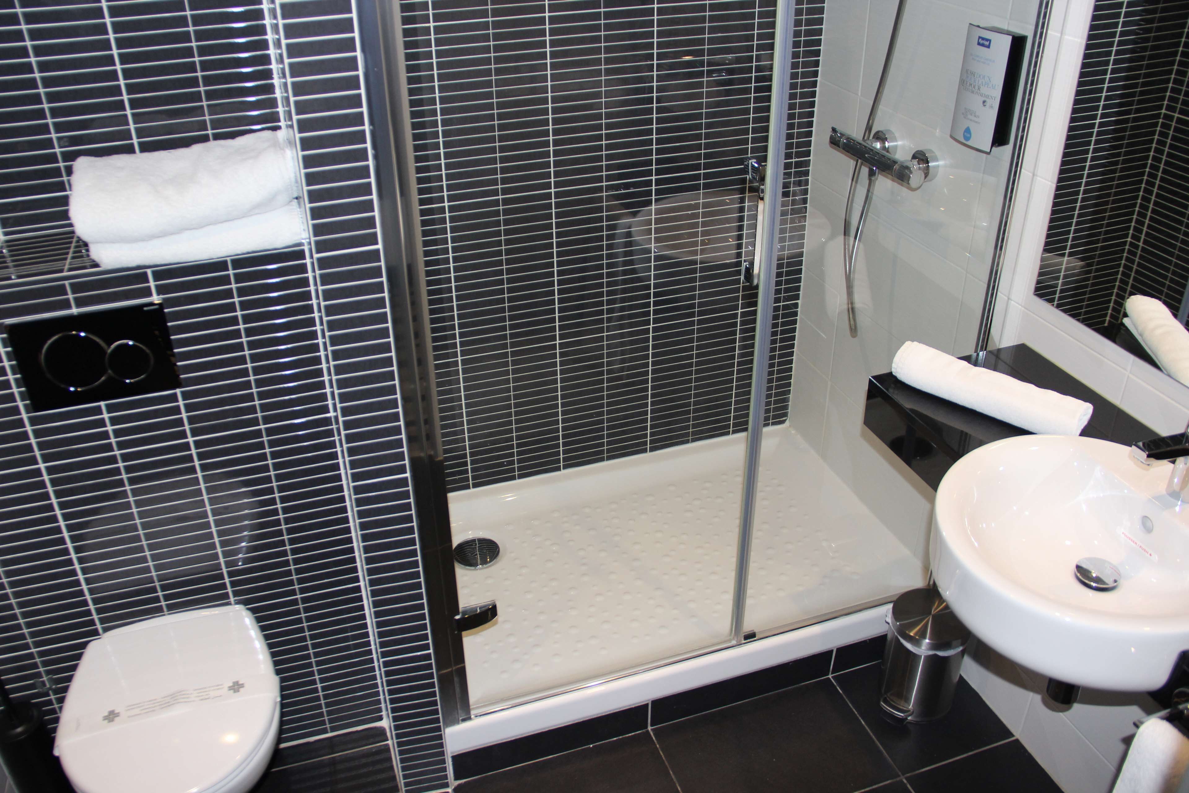 Une salle de bain moderne avec une douche à parois de verre, des toilettes blanches et un lavabo avec un miroir.