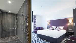 A modern hotel room with a shower area, a large bed with a headboard, a nightstand, and a seating area with a sofa. - Hôtel Kyriad Saint Quentin en Yvelines - Montigny (Montigny-le-Bretonneux)
