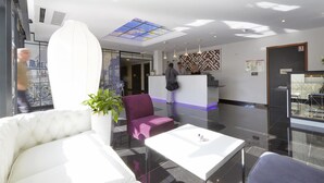 A modern hotel lobby with a reception desk, seating area, and a large window with a view. - Hôtel Kyriad Saint Quentin en Yvelines - Montigny (Montigny-le-Bretonneux)