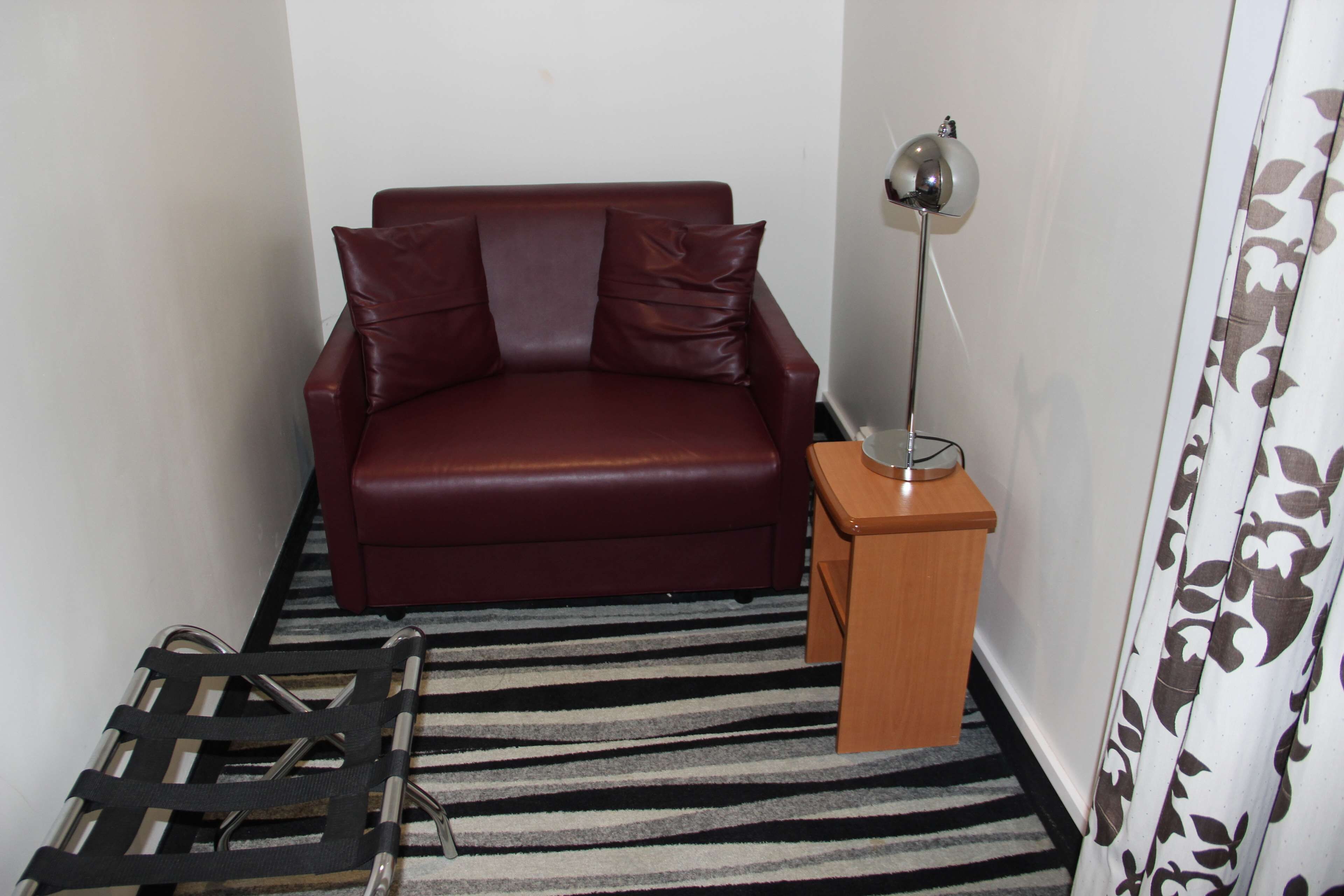 A small room with a red sofa, a wooden side table, a floor lamp, and a striped rug.