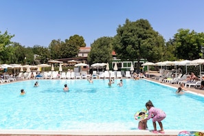 A swimming pool with lounge chairs and umbrellas, surrounded by trees and buildings.