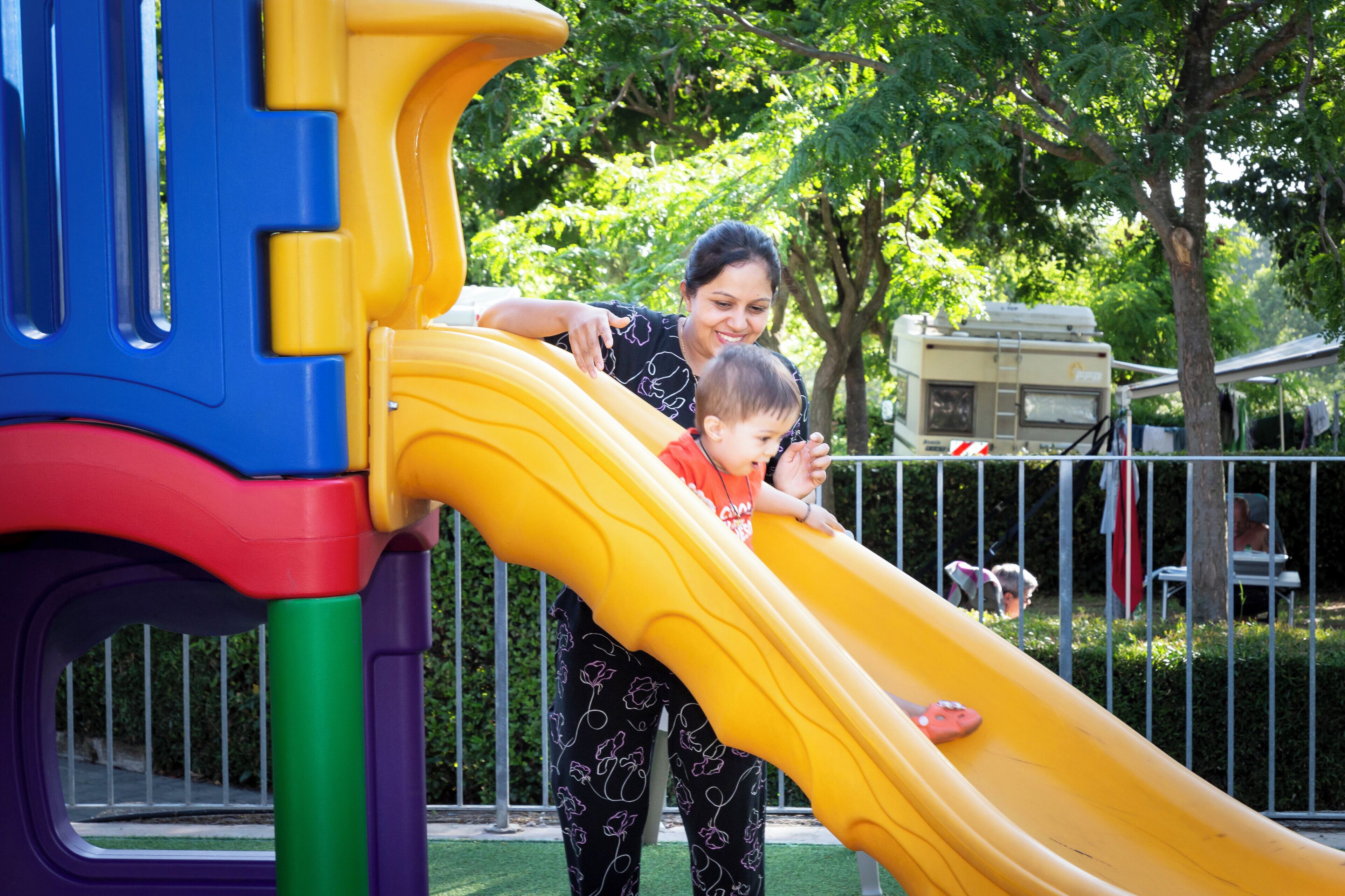Un parque infantil con un tobogán amarillo y una mujer y un niño en la parte superior.
