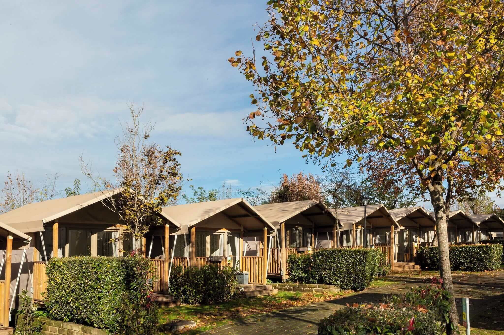Une rangée de cabanes en bois aux toits en pente, entourées de haies et d’arbres bien entretenus.