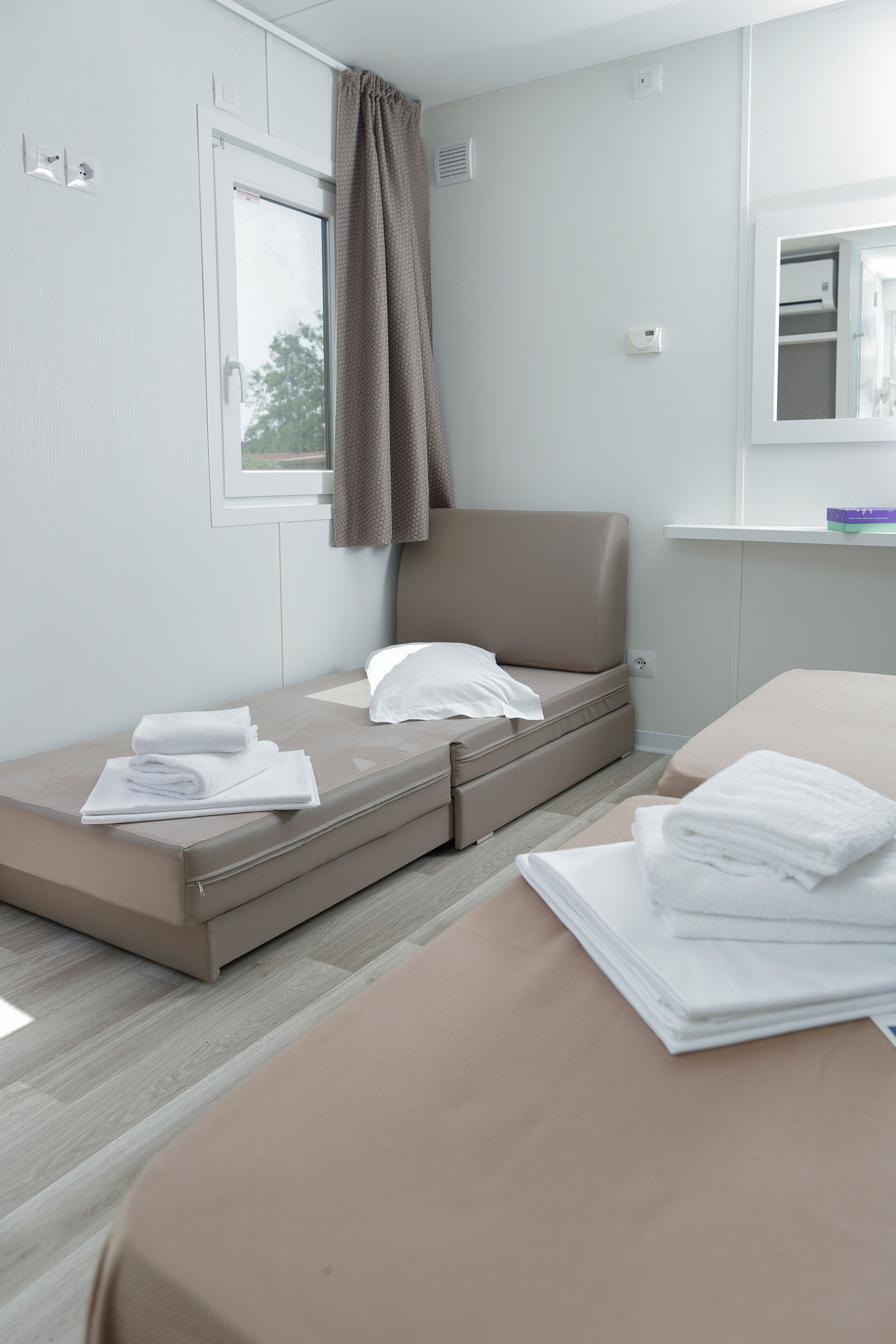 A compact hotel room with a single bed, a small sofa bed, and a window with curtains.